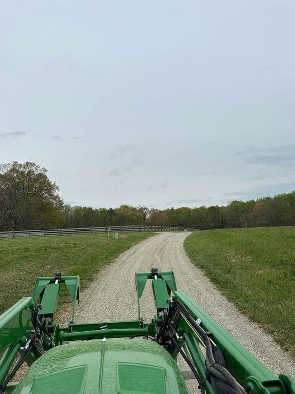 View from a green tractor driving on a gravel road through lush, green fields.