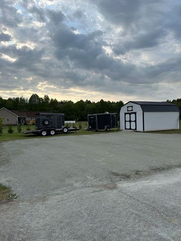 Black trailers parked next to a gray storage shed under a cloudy sky. Rural setting.