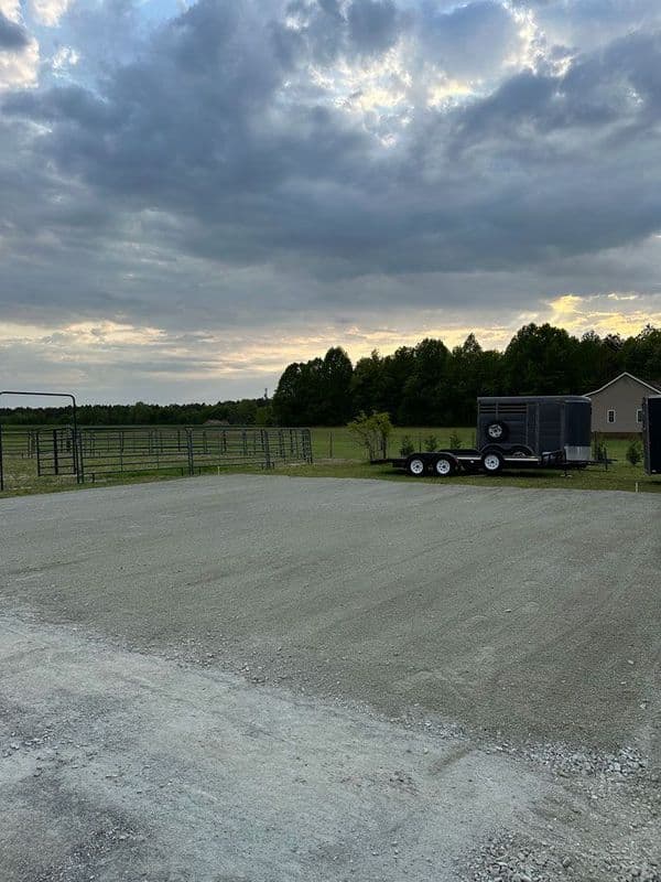 Gravel lot with a trailer under a cloudy sky and green trees in the background.
