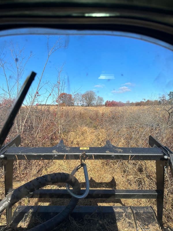 View from a tractor's cabin showing farmland and blue sky during autumn.