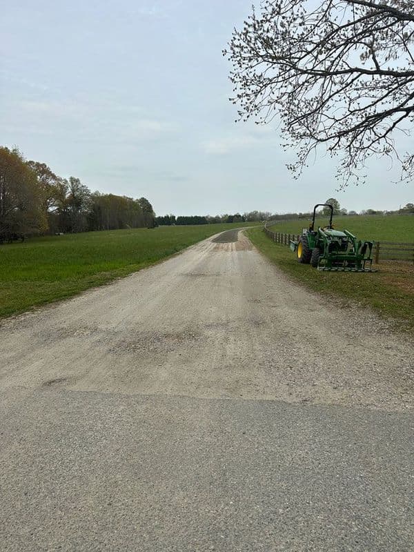 Gravel road lined with greenery and a green tractor in a rural landscape.