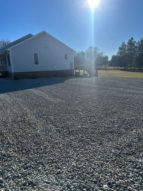 Gravel driveway leading to a home with sunlight and trees in the background.