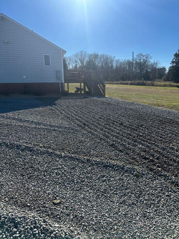 Gravel yard beside a house with a deck under a clear blue sky.