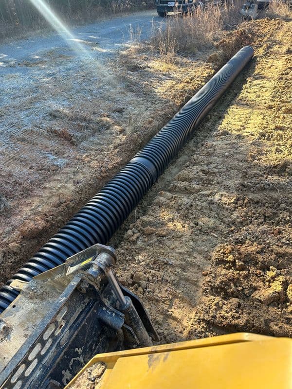 Black drainage pipe installation on a construction site, surrounded by freshly dug earth.