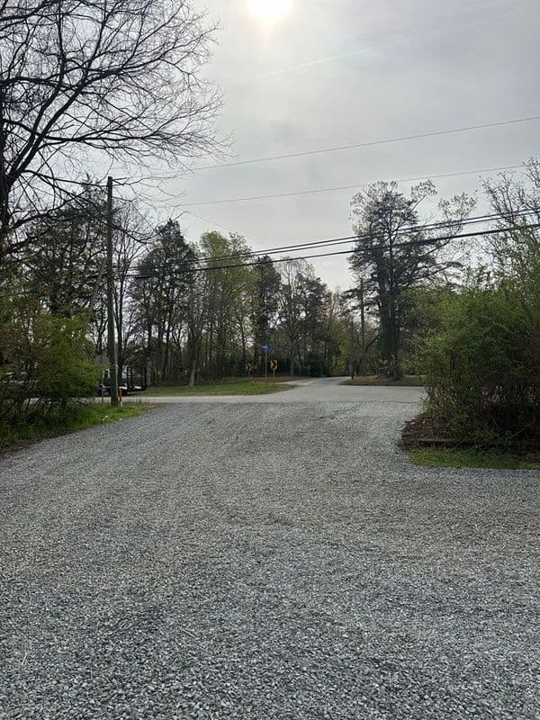 Gravel road intersection surrounded by trees under a cloudy sky.