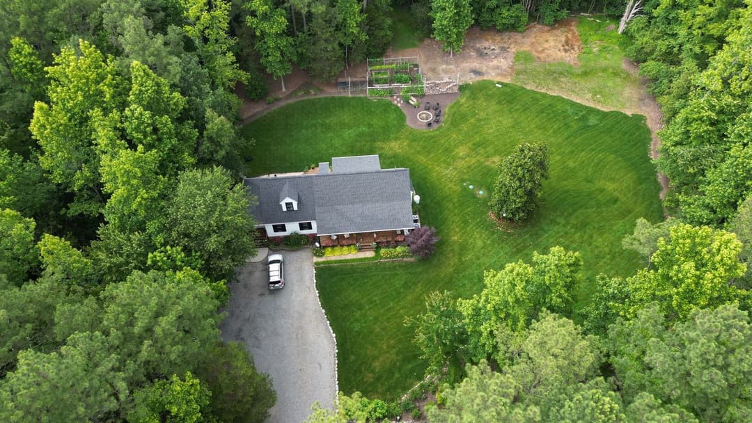 Aerial view of a house surrounded by lush green trees and a well-maintained lawn.
