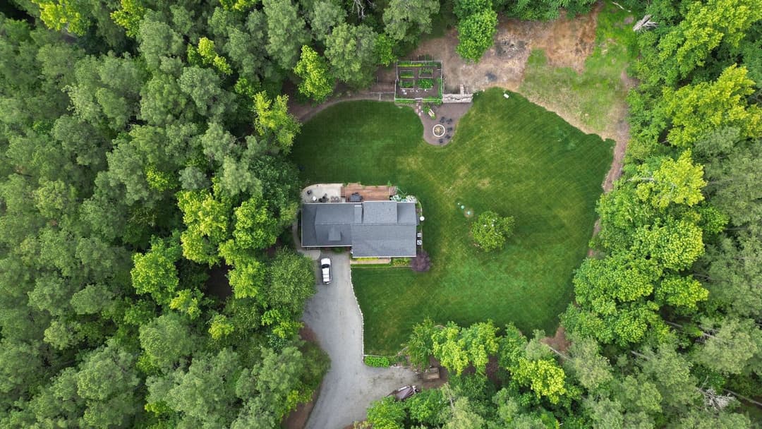 Aerial view of a house surrounded by lush greenery and meticulously landscaped lawn.
