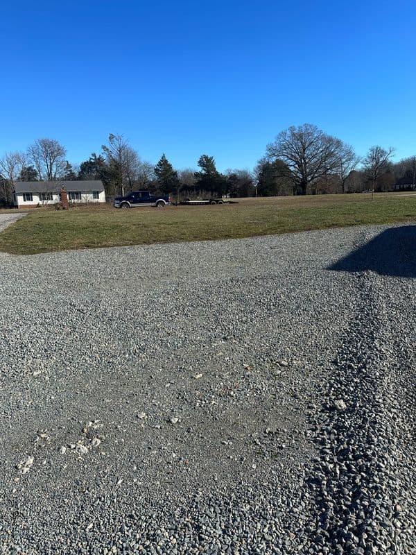 Gravel lot with a house and truck under a clear blue sky.